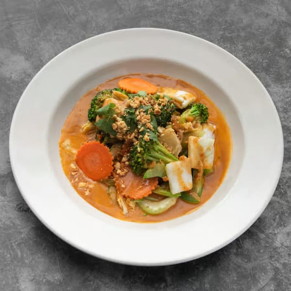 Mai Thai red curry with broccoli, carrots, tofu, and crushed peanuts in a white bowl.