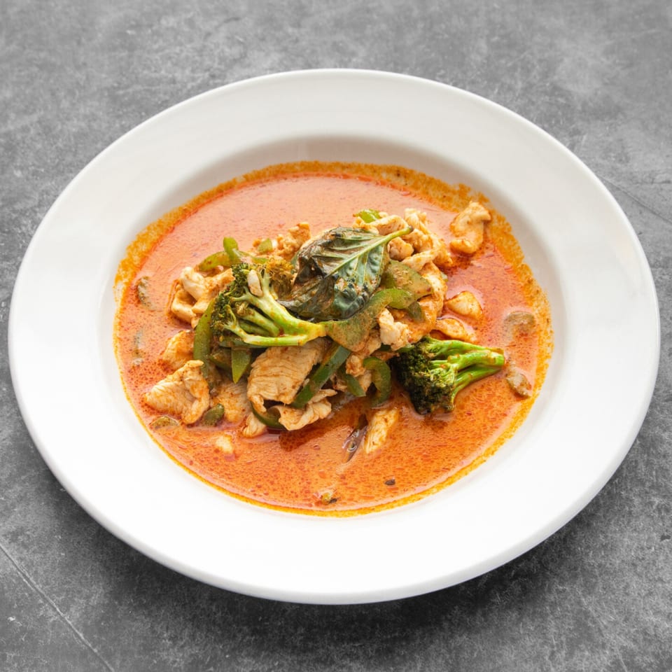 Mai Thai Restaurant's red curry with chicken, broccoli, bell peppers, and basil in a white bowl.