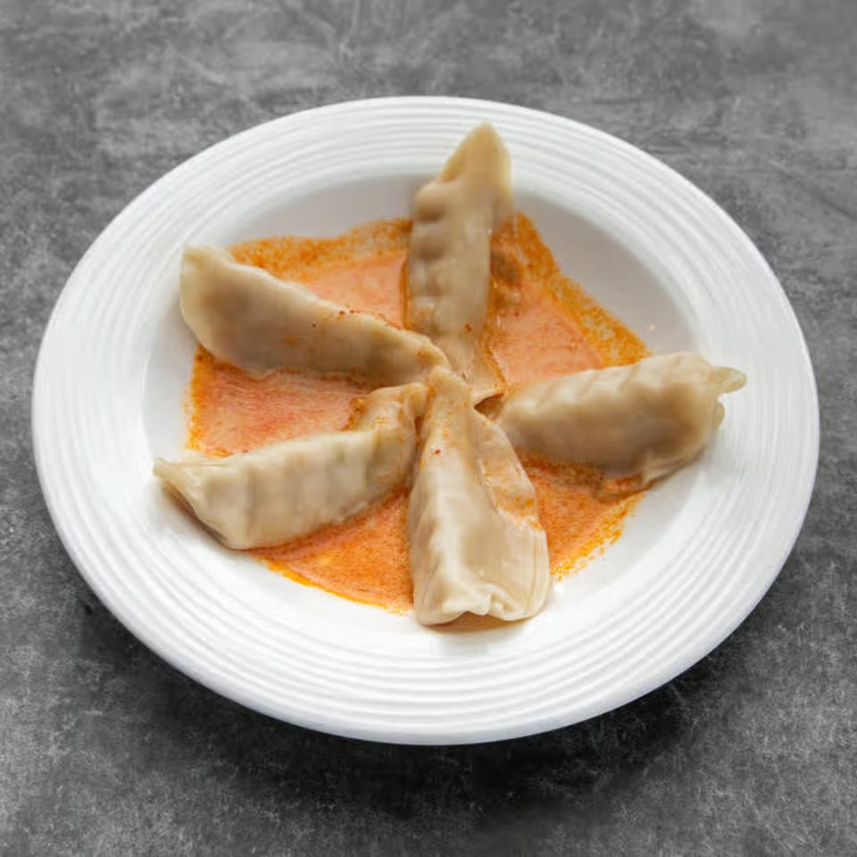 Five Thai dumplings arranged in a star shape on a white plate with orange sauce.