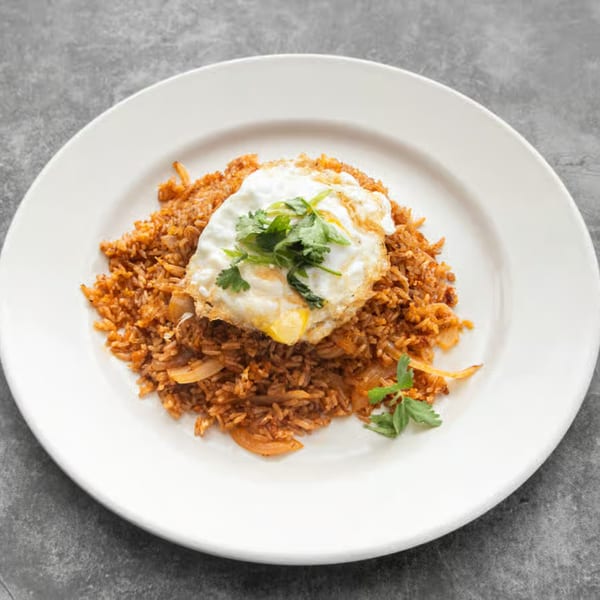 Thai fried rice with onions, topped with a fried egg and fresh cilantro on a white plate.