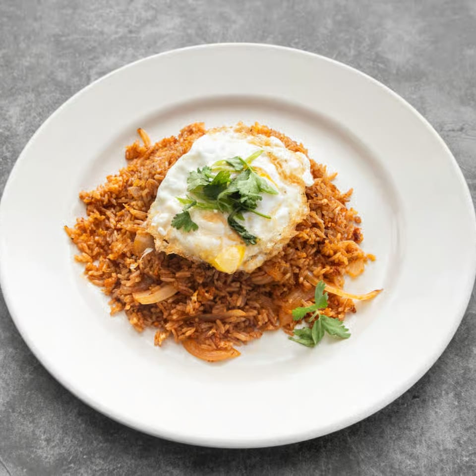 Thai fried rice with onions, topped with a fried egg and fresh cilantro on a white plate.